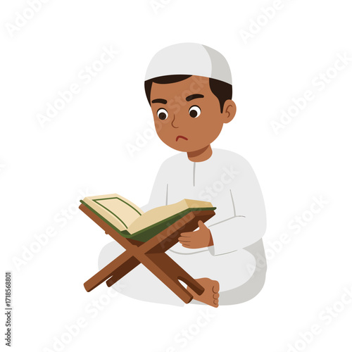A young boy wearing a white kufi and thobe sits cross-legged, attentively reading from an open book on a wooden stand.
