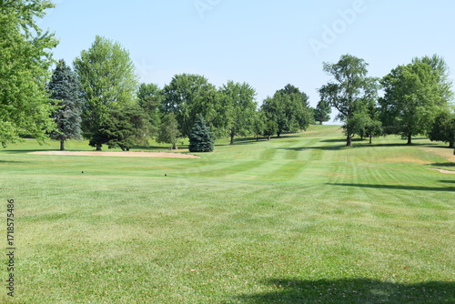 Looking down a tree lined golf course fairway towards the putting green.