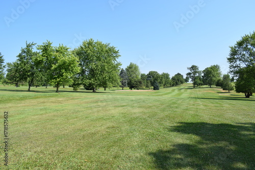 Looking down a tree lined golf course fairway towards the putting green.
