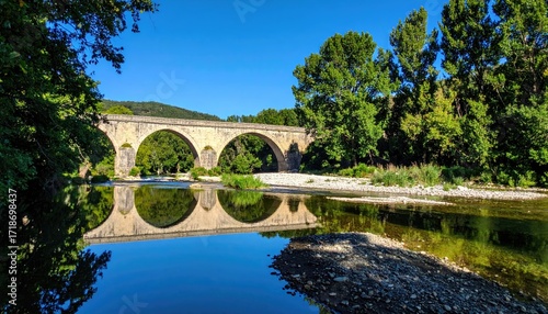 Stone arch bridge over tranquil river, reflected in calm water, framed by trees