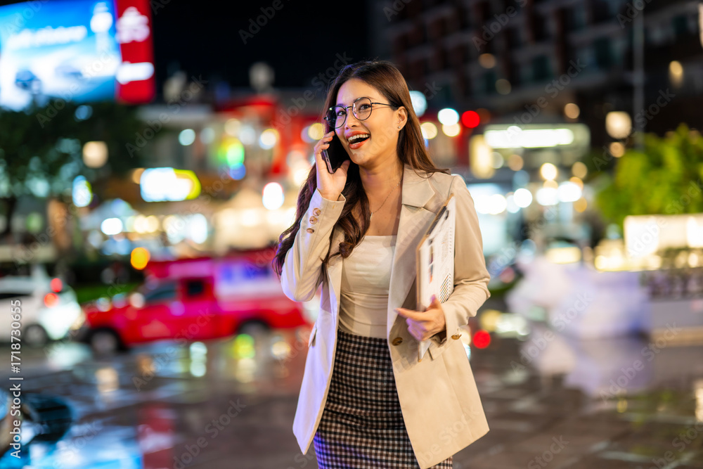 Fototapeta premium Businesswoman walking and talking on phone in city at night