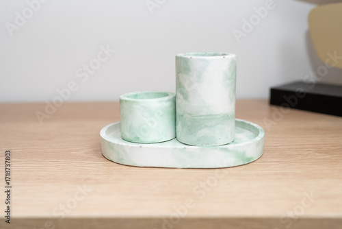 Three elegant marble candle holders in varying heights are placed on a circular tray. The soft green and white colors contrast beautifully with the light wooden surface.
