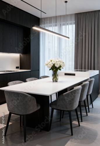 Minimalist dining room with white flowers centerpiece, gray chairs, black table, modern pendant light, sheer curtains, natural light.