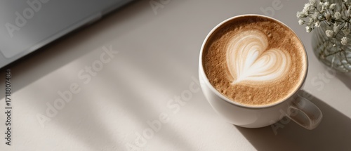 Flat lay of a white coffee cup with heart-shaped foam placed on a sleek workspace in neutral tones with minimal decor, perfect for mindfulness routines, productivity content, and remote work visuals.
