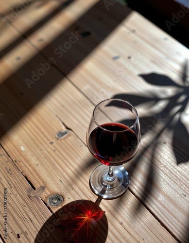 Elegant glass of red wine on rustic wooden table with natural sunlight casting shadows, showcasing warm cozy atmosphere perfect for relaxation or dining