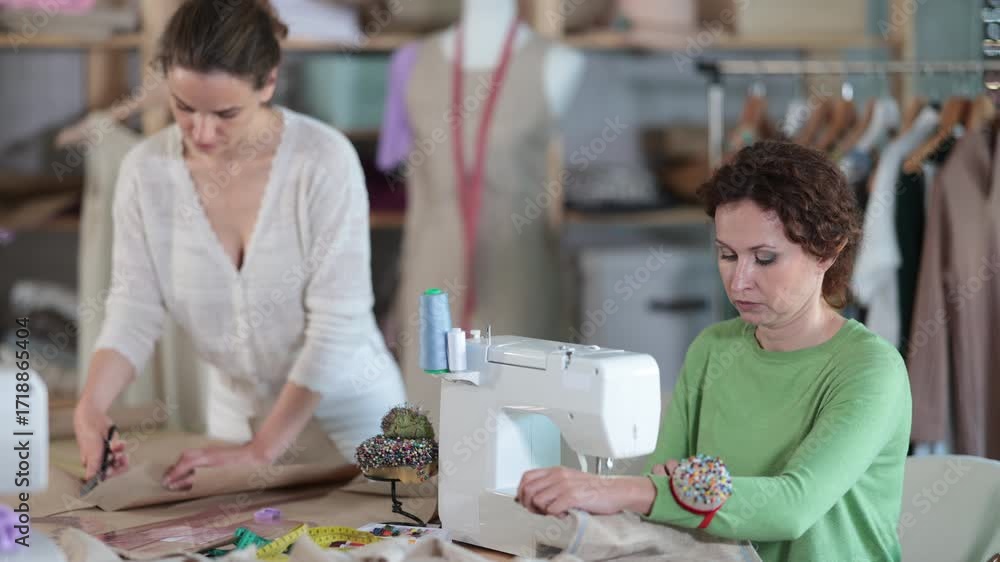 Woman designer sews clothes using sewing machine, perform edge finishing stitching seam. Apprentice cut out paper dress pattern