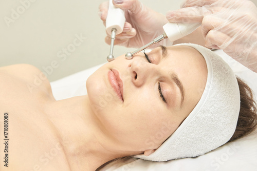 Young caucasian female receiving facial treatment with microcurrent therapy in spa.