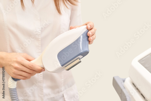 Caucasian female technician holding hair removal device for laser skin treatment in clinic.