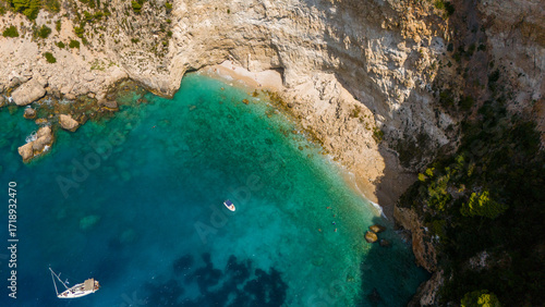 Fototapeta Naklejka Na Ścianę i Meble -  Filippoi beach aerial view with steep rocky cliffs turquoise water boats anchored near shore and dense green forest covering the surrounding hills