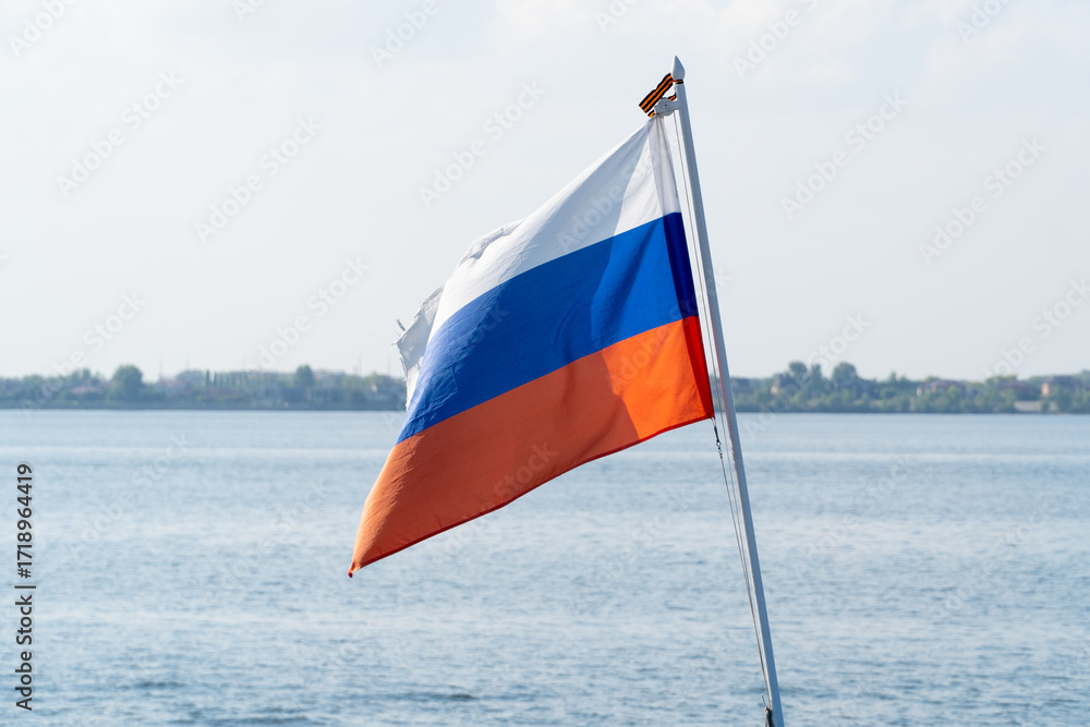 Naklejka premium The Russian flag flutters in the wind against the blue sky. The national flag of Russia waving in the wind on a clear day. White, blue and red horizontal stripes. Russian Federation flag. 