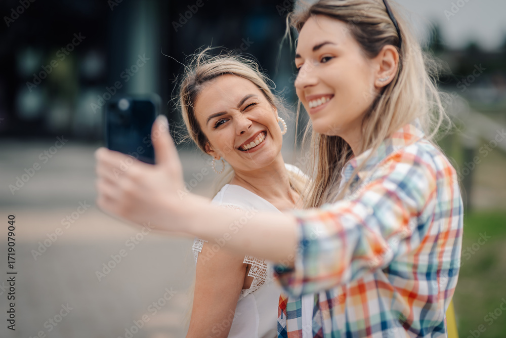 Obraz premium Two smiling women taking a selfie with smartphone outdoors