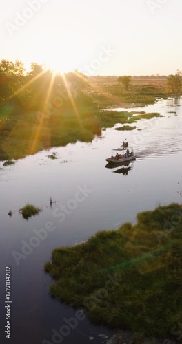 Vertical panning aerial video. Tourists on a sightseeing boat on a river in the Okavango Delta at sunset