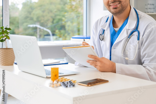 Male doctor writing in note...
