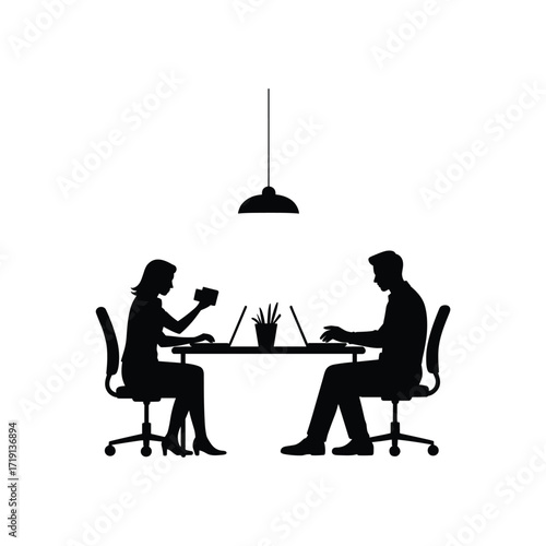 Silhouette of a man and woman working on laptops at a table under a pendant lamp