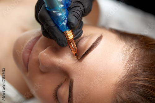 Close-up of eyebrow tattooing process showing artist's hand creating defined brows on client in a beauty studio