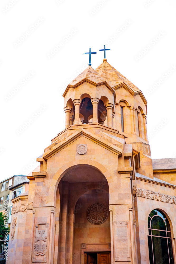 Fototapeta premium Beautiful close-up of a golden stone Armenian church in Yerevan, featuring twin towers with crosses, detailed carvings, and elegant arches. A striking example of Armenian Christian architecture