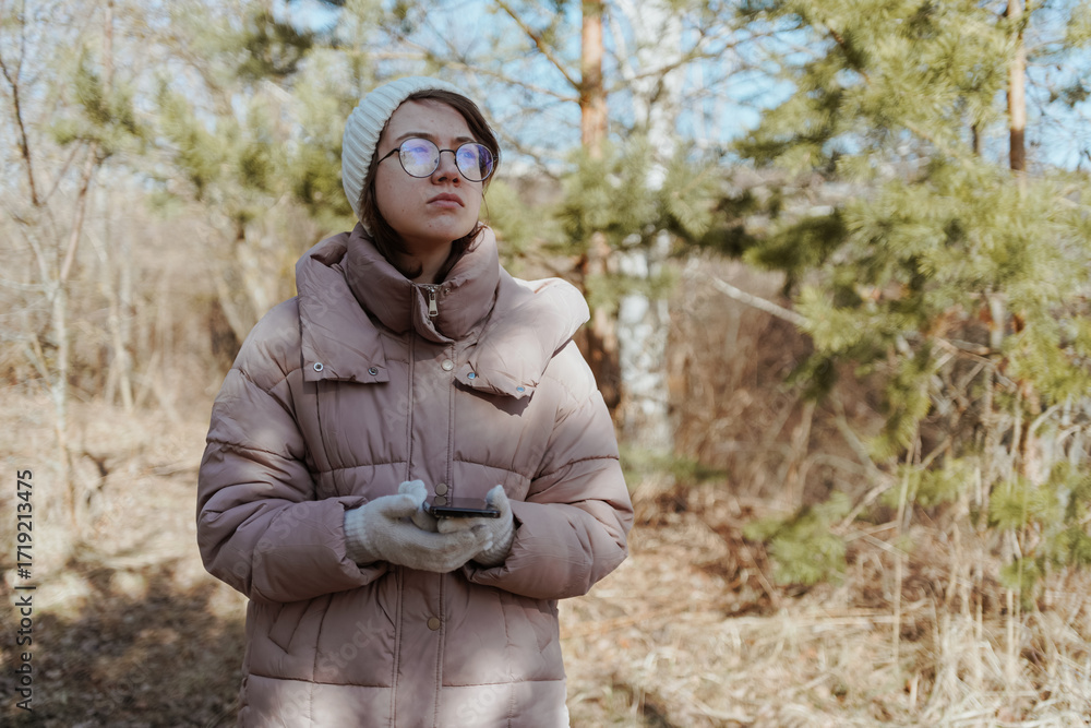 Fototapeta premium A young woman in a park uses her phone to navigate, enjoying nature while finding her way. Captures modern exploration, relaxation, and technology in daily life