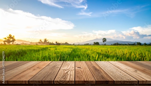 Wooden plank table in foreground with lush green rice field and blue sky with clouds in background during sunrise