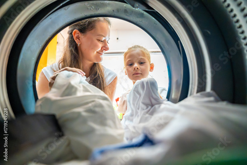 Mother and daughter doing laundry together in a self-service public laundromat, sharing household chores, building responsibility and cooperation in everyday family routine