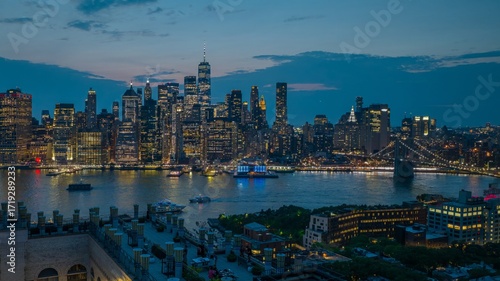Aerial view of the vibrant city lights reflecting on the river as the One World Trade Center stands tall against the darkening sky, Manhattan, New York, United States.