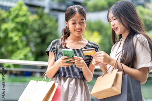 Fotografía Two asian woman shopping outdoors using credit card and smartphone for mobile pa