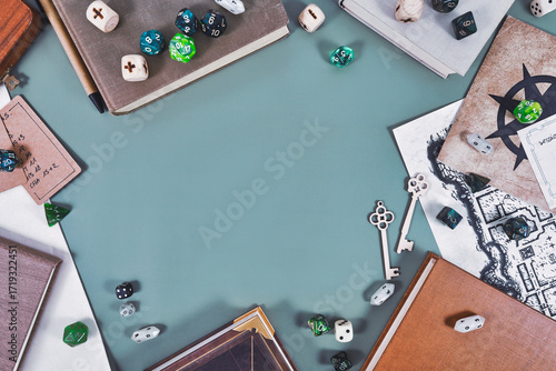 Tabletop role playing flat lay background with colorful RPG dices, rule books, dungeon map forming frame around blue negative space