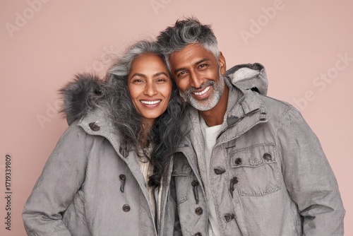 Portrait of a satisfied indian couple in their 40s wearing a lightweight packable anorak in front of pastel or soft colors background