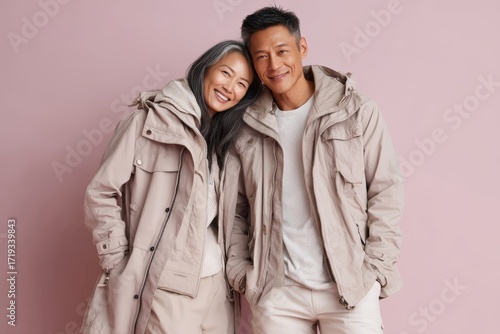 Portrait of a cheerful asian couple in their 40s wearing a lightweight packable anorak in pastel or soft colors background