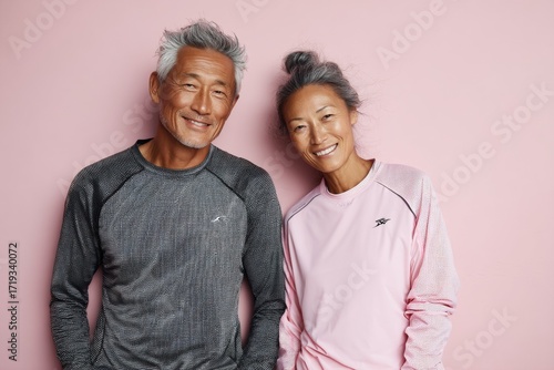 Portrait of a blissful asian couple in their 70s wearing a moisture-wicking running shirt in pastel or soft colors background