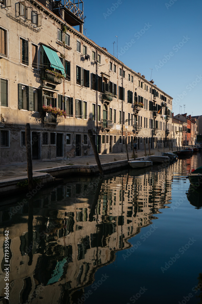 Obraz premium Historic Venetian houses reflecting in the calm canal water at sunset, creating a mirror-like scene that emphasizes the timeless beauty and architectural harmony of Venice