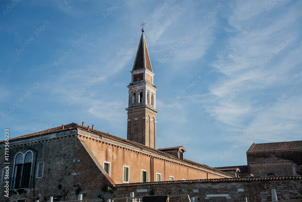Fototapeta premium Scenic view of church tower in Venice with rustic architecture, sloped terracotta roofs and cultural heritage buildings against bright summer sky in Italy