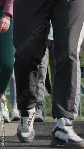 Lower angle view capturing feet in sneakers as people in joggers walk into sports court, detailed with green gate and chairs with bags, ready for activity