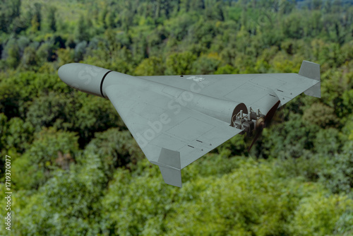 A military unmanned aerial vehicle flies over a green forest on a clear day.