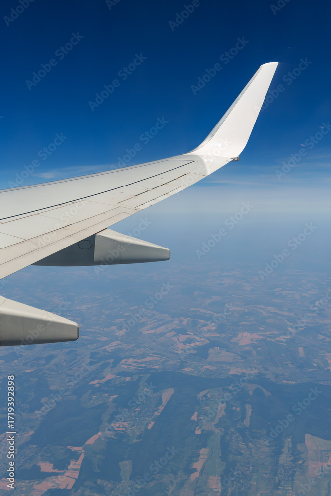Naklejka premium view from airplane window on wing and landscape below, horizon above planet and air haze, airplane view