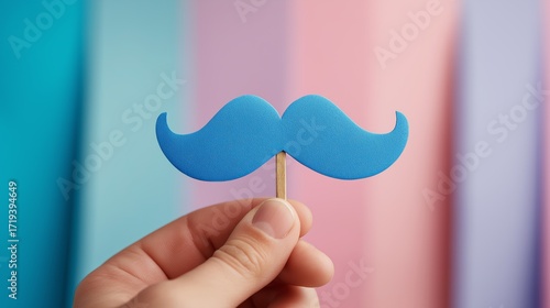 blue paper mustache prop held by hand for men’s health awareness visuals, social campaigns, and Movember promotional materials, colorful pastel background, studio shot, playful layout, centered object
