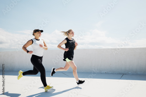 Fotografija Two women running together on a rooftop track during a sunny day