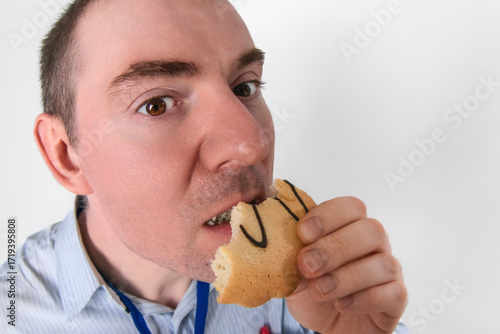 Office worker, man eating a cookie. Close-up wide-angle facial portrait