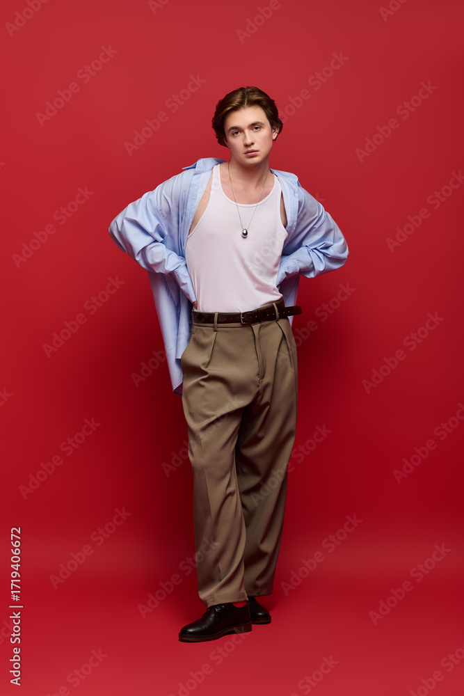Fototapeta premium Stylish young man showcases trendy outfit against vibrant red backdrop