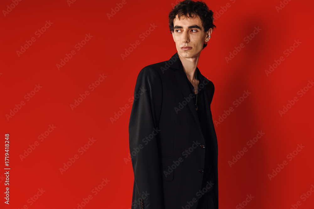 Obraz premium Handsome man showcasing elegant style against vibrant red backdrop in a modern fashion setting