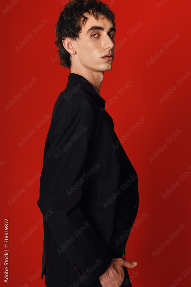 Obraz premium Handsome stylish man in elegant attire poses confidently against a vibrant red background