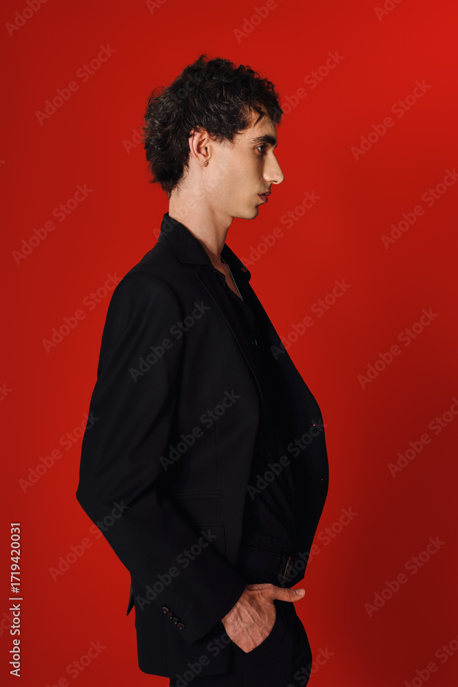 Obraz premium Handsome man showcases elegant fashion against a striking red backdrop