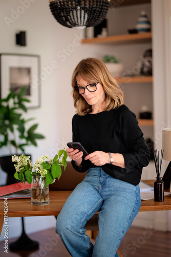 Blond haired confident woman sitting at desk at home and using her smartphone
