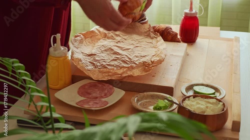 Female hands wrap croissant sandwich into wrapping paper close up