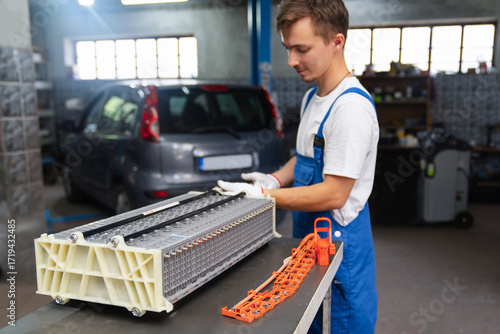 Serviceman replacing hybrid electric vehicle battery pack in workshop