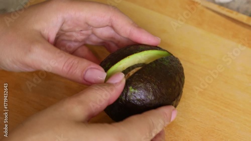 Female hands cutting in halves fresh green avocado with knife on cutting board close up