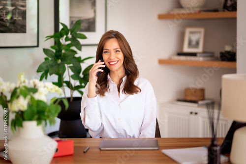 Happy middle-aged woman sitting at home and using smartphone and laptop