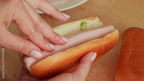 Female hands putting sausage on a bun during hot dog cooking close up