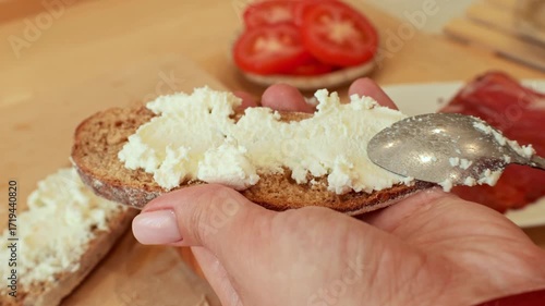 Female hands spreading soft ricotta cheese on bread during sandwich cooking close up