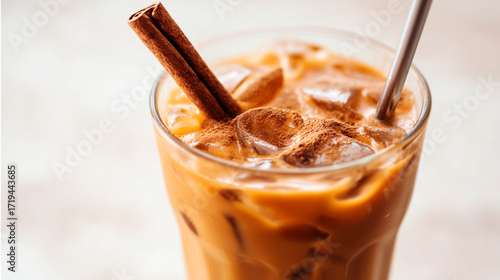 Fototapeta Naklejka Na Ścianę i Meble -  Iced pumpkin spice latte with cinnamon stick garnish in glass mug with metal straw. Cold fall coffee drink with creamy milk and seasonal spices for autumn cafe.