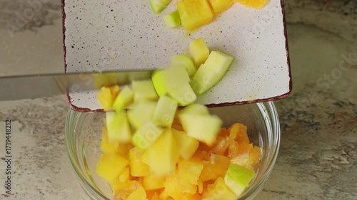 Female hands putting sliced fruits for fruit salad with knife into a bowl close up
